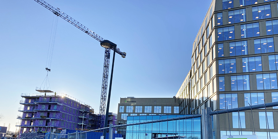 Stor kontorsbyggnad mot en blå himmel. En lyftkran och en mindre byggnad som håller på att byggas syns också.