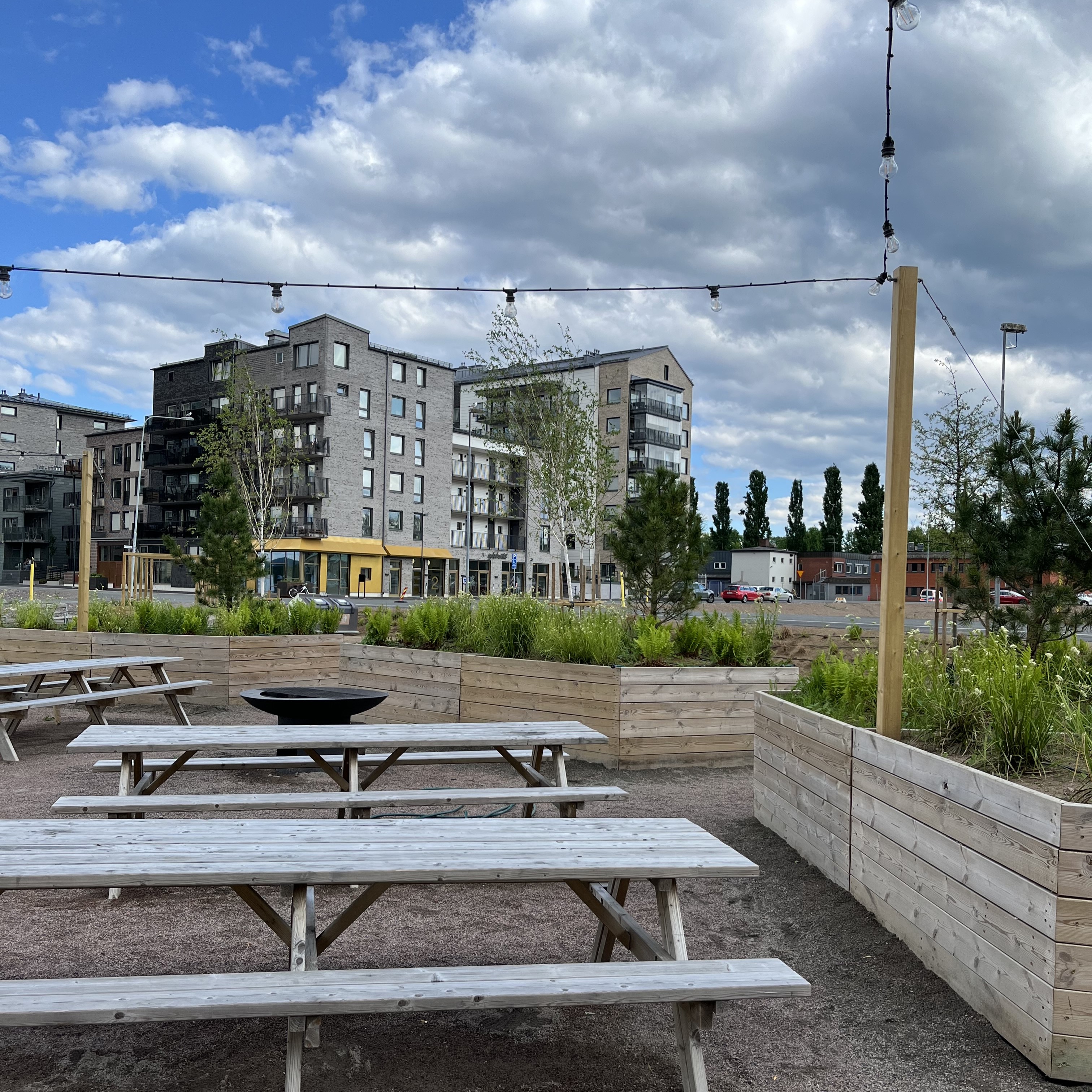 En grönskande park med träbänkar. I bakgrunden syns kvarter 8