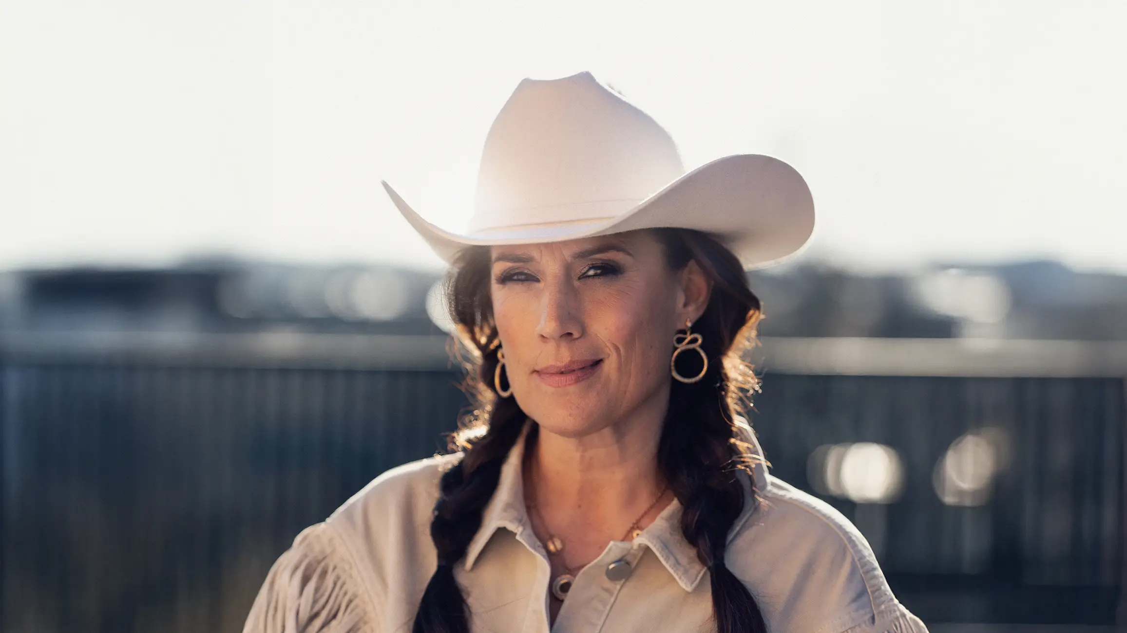 Brunhårig kvinna i vit cowboyhatt och vit jacka med fransar. 