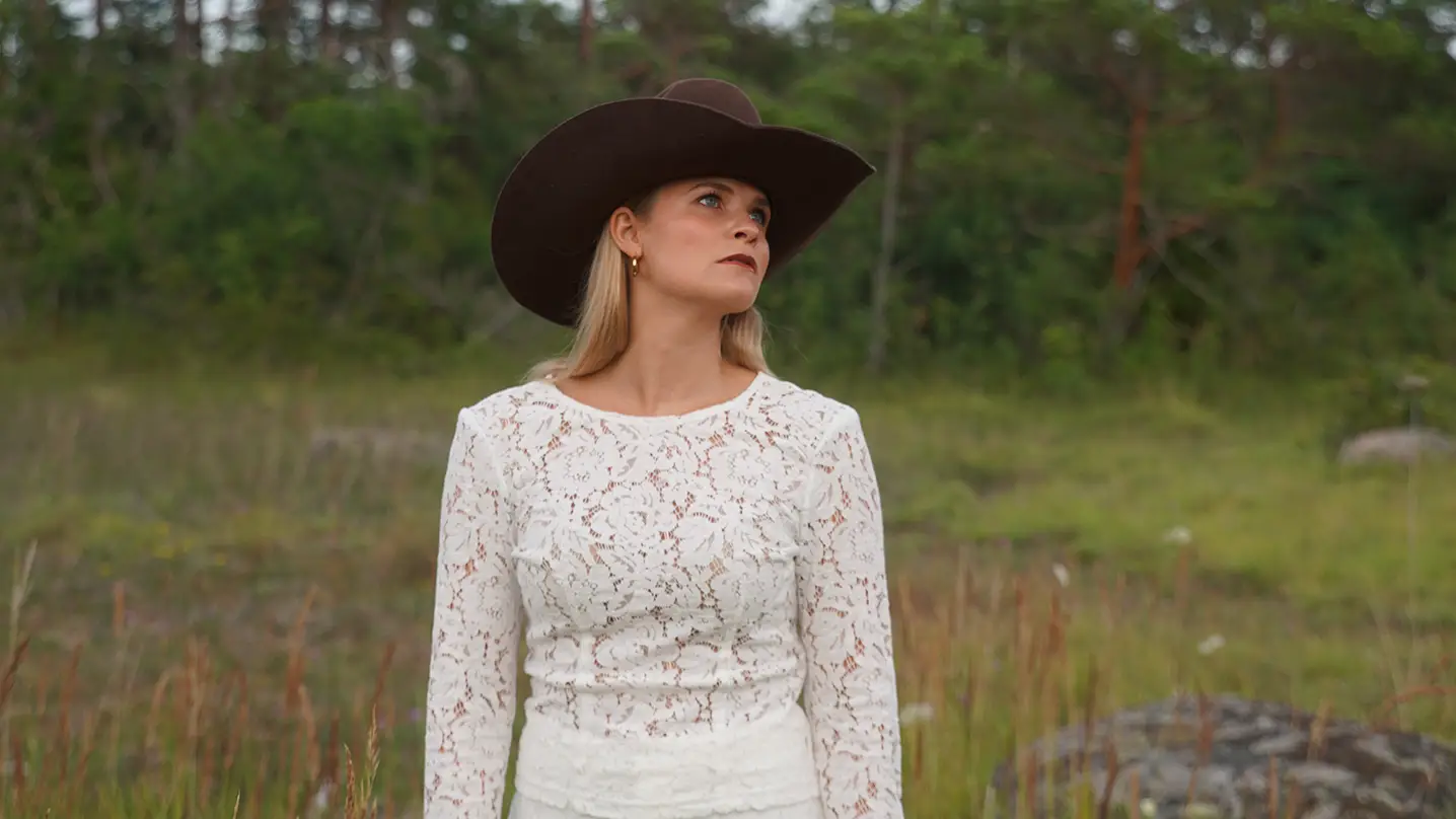 En kvinna i vita kläder och brun cowboyhatt.