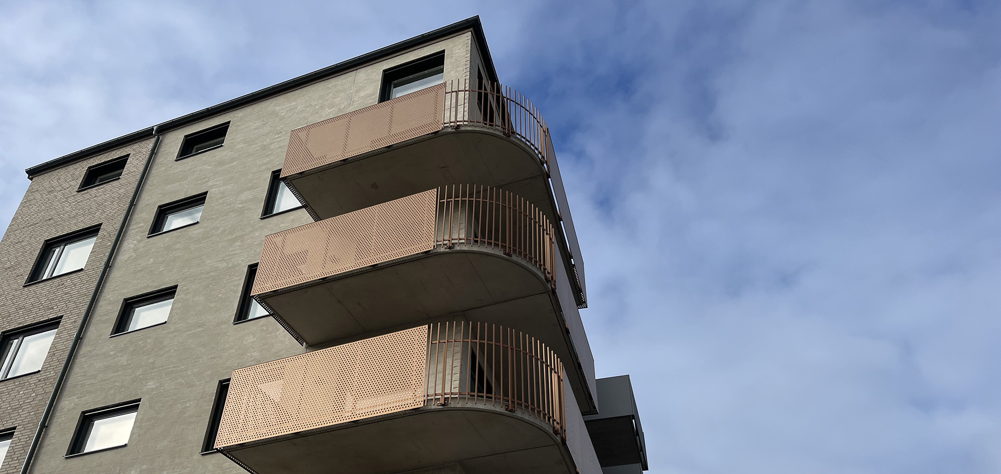 Husgavel mot blå himmel. Huset är i ljust tegel och gaveln har orange, rundade balkonger.