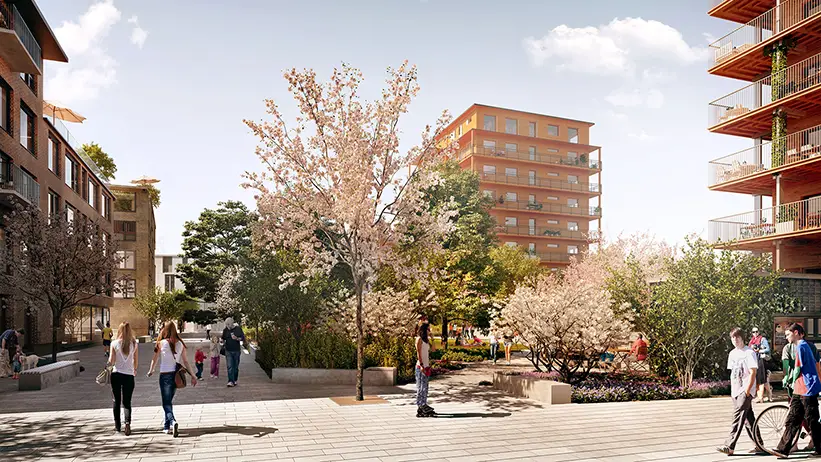 Grönskande park med planteringar. Utanför ligger stenläggning där människor rör sig. 