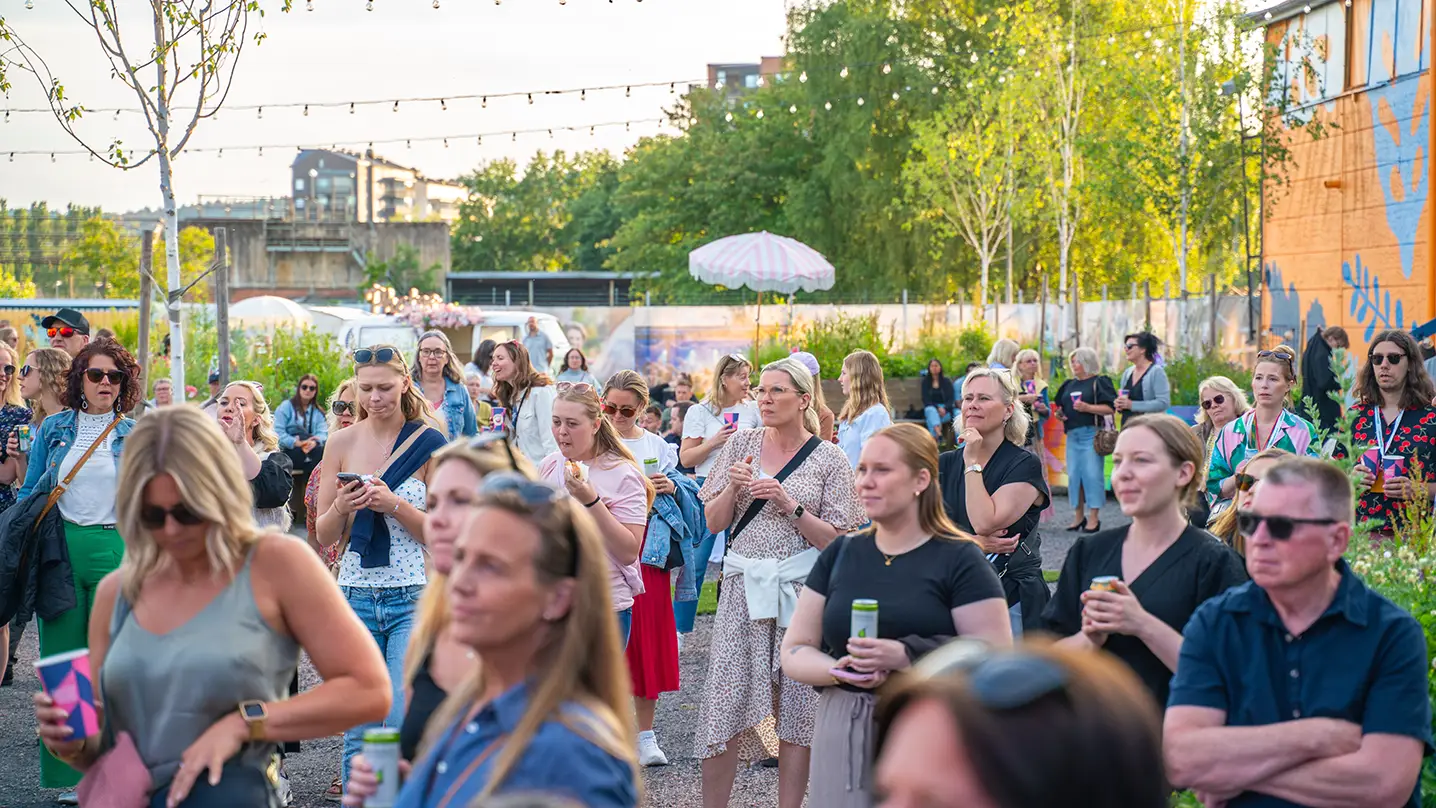 Ett folkhav av sommarklädda människor står på en grön innergård.