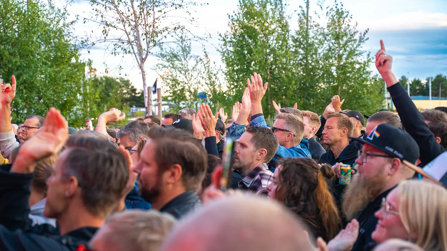 Ett folkhav sträcker händerna i luften. I bakgrunden syns gröna träd.