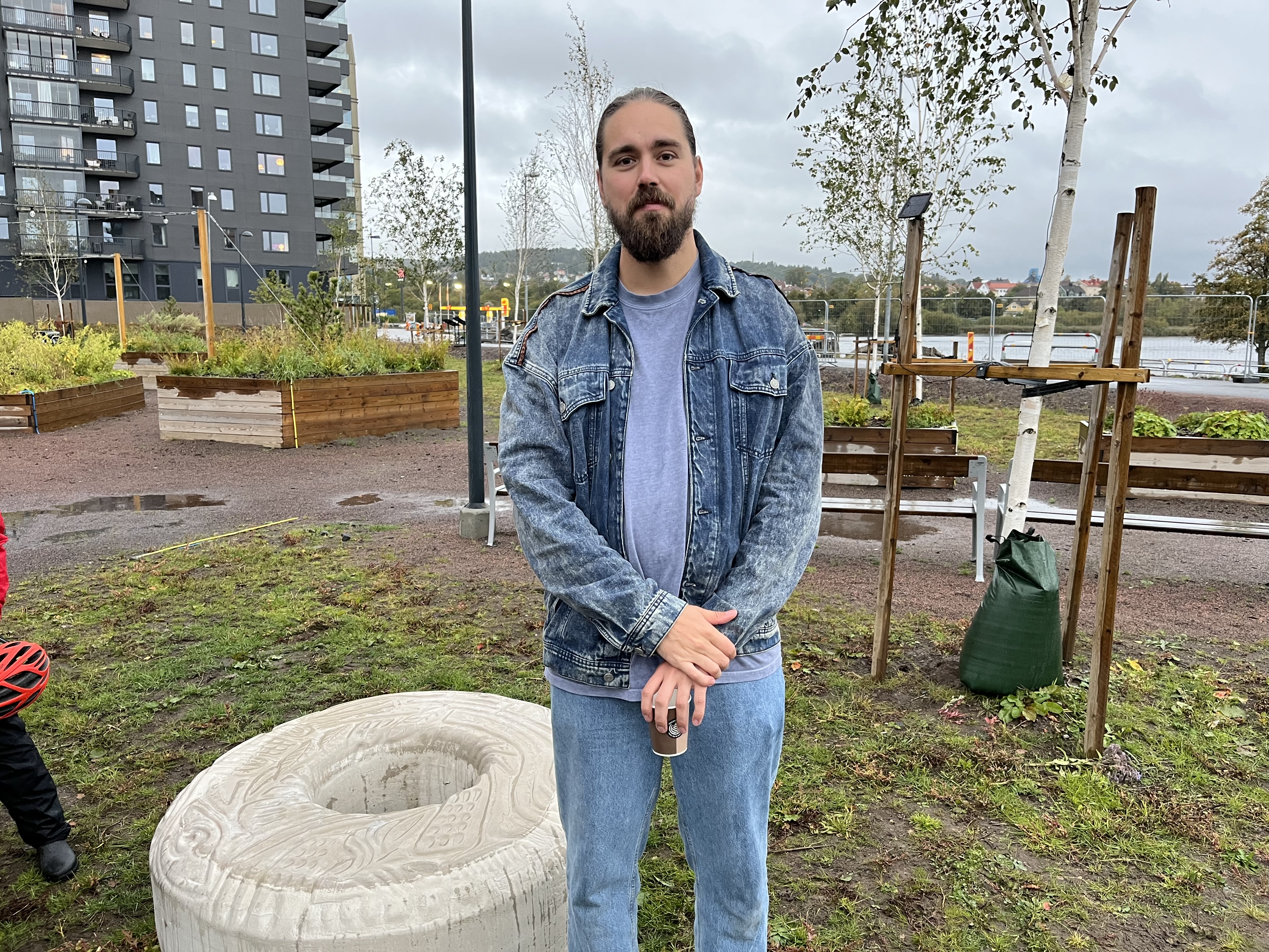 Konstnären är klädd i jeansjacka och står framför sina konstverk.
