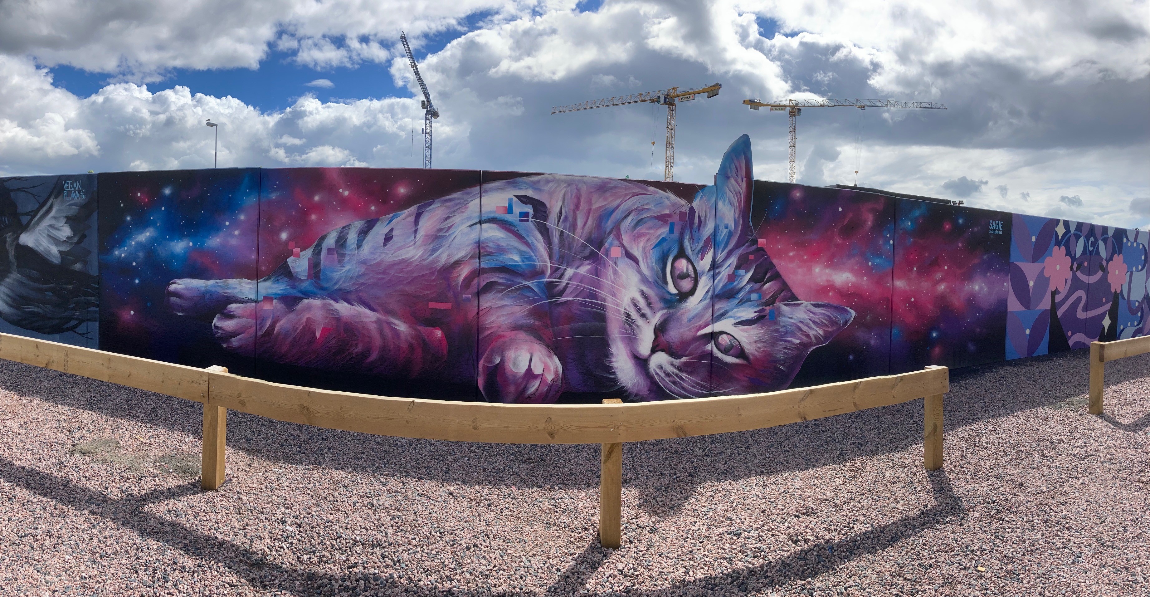 En tio meter lång muralmålning på betongväggen föreställande en rosa och lila katt med ränder som ligger på sidan.