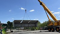 En gul kranbil lyfter plåtbyggnaden som händer ett par meter ovanför marken inne på innergården.