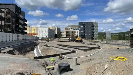 Byggarbetsplats, en stor sandad yta med bostadshus i bakgrunden.