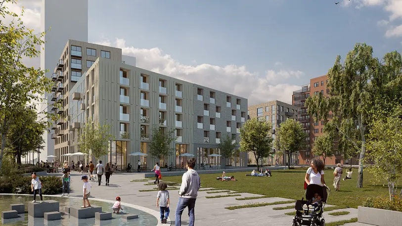 En grön park med människor som rör sig. I bakgrunden syns bostadshus i olika höjder.