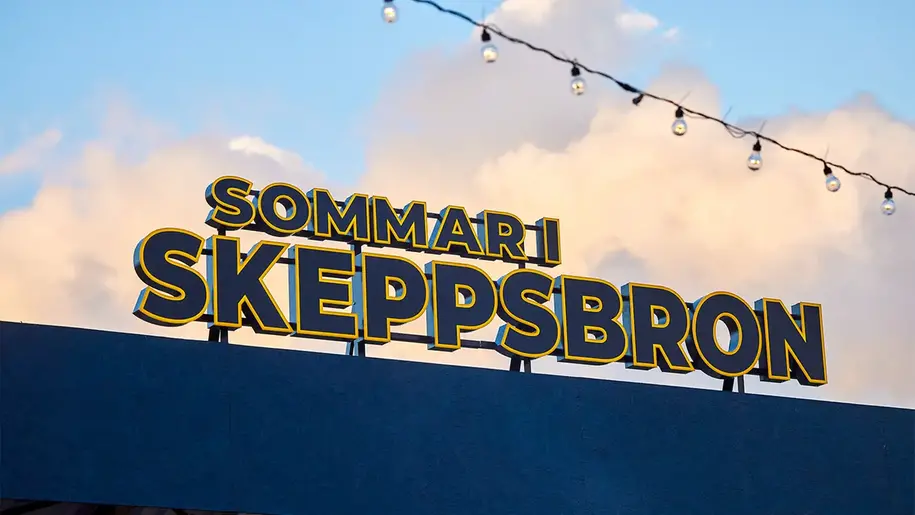 Bild på LED-skylt där det står Sommar i skeppsbron. Bakom skylten syns en blå himmel med moln.