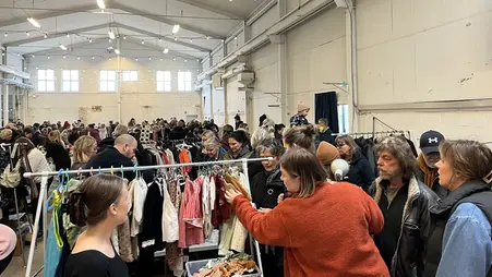 Människor i ett stort rum. En kvinna i röd jacka tittar bland kläderna på en klädställning.