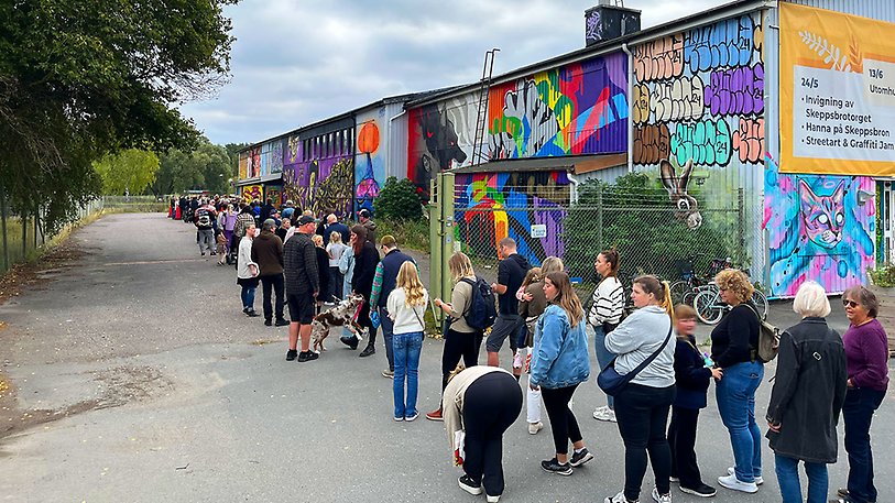 Människor står i en lång kö utanför ett hus som är målat med grafitti